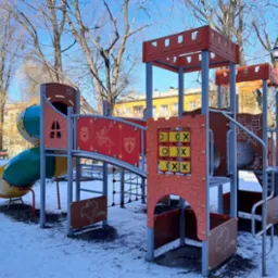 Kolorowy zestaw zabawowy na zewnątrz z tunelem, zjeżdżalnią i elementami do wspinaczki, otoczony śniegiem w słoneczny dzień.