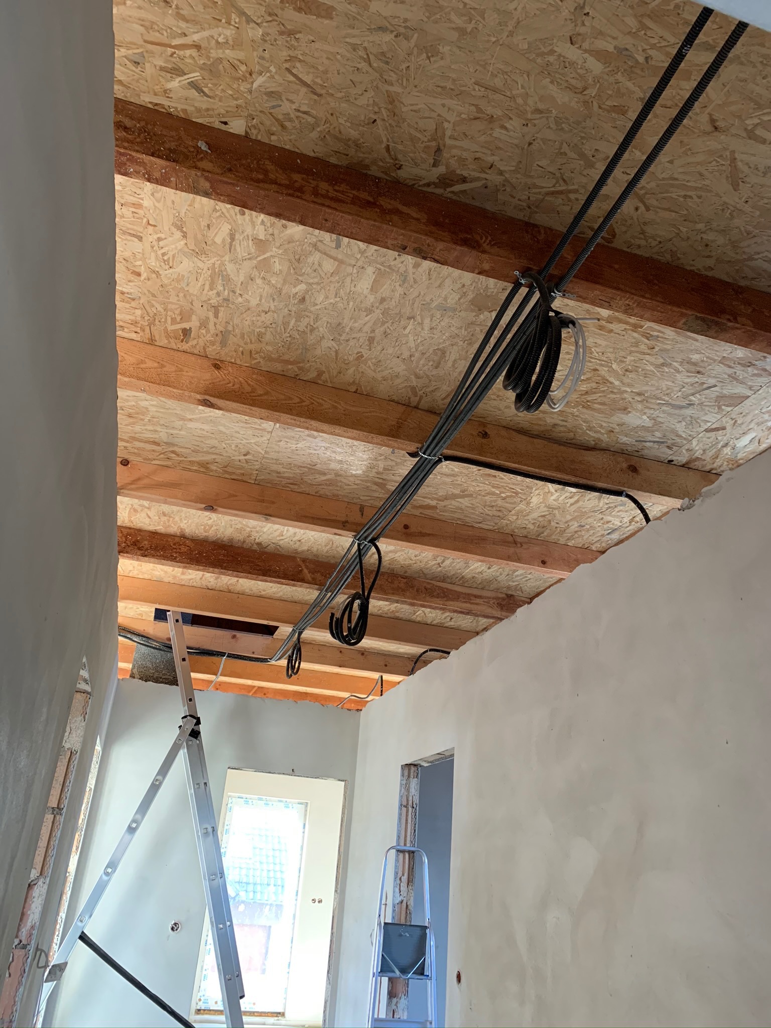 Instalacja przewodów elektrycznych pod stropem z płyt OSB w domu w Gogolinie, widoczna drabina i surowe ściany.
