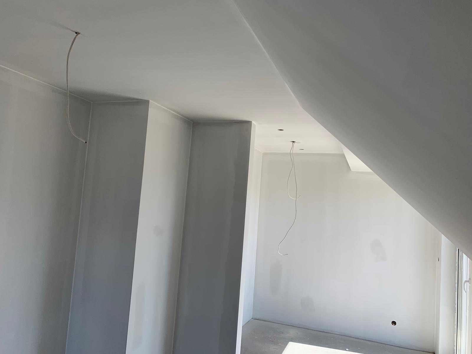 Poddasze w trakcie wykańczania: szpachlowane ściany, sufit ze skosem, wystające przewody elektryczne przed malowaniem.