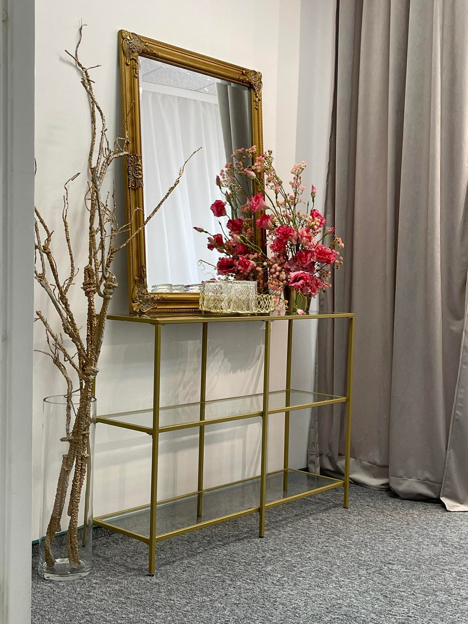 Dekoracyjny stolik konsolowy z lustrem w złotej ramie, bukietem czerwonych kwiatów i suchymi gałązkami w wazonie, aranżacja wnętrza w Rzeszowie.