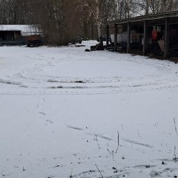 Osoba prywatna - Zimowy plac z zaparkowanym autobusem i kamperem pod zadaszeniem, widoczne ślady opon na śniegu.