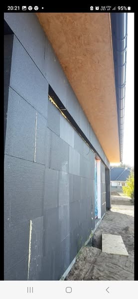 Elewacja budynku w trakcie ocieplania styropianem grafitowym, widoczne fragmenty pianki montażowej i przygotowane otwory okienne.