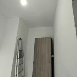 Wnętrze po malowaniu na biało, widoczna drabina aluminiowa, zamontowane drzwi z okleiną drewnopodobną oraz fragment surowego muru w rogu.