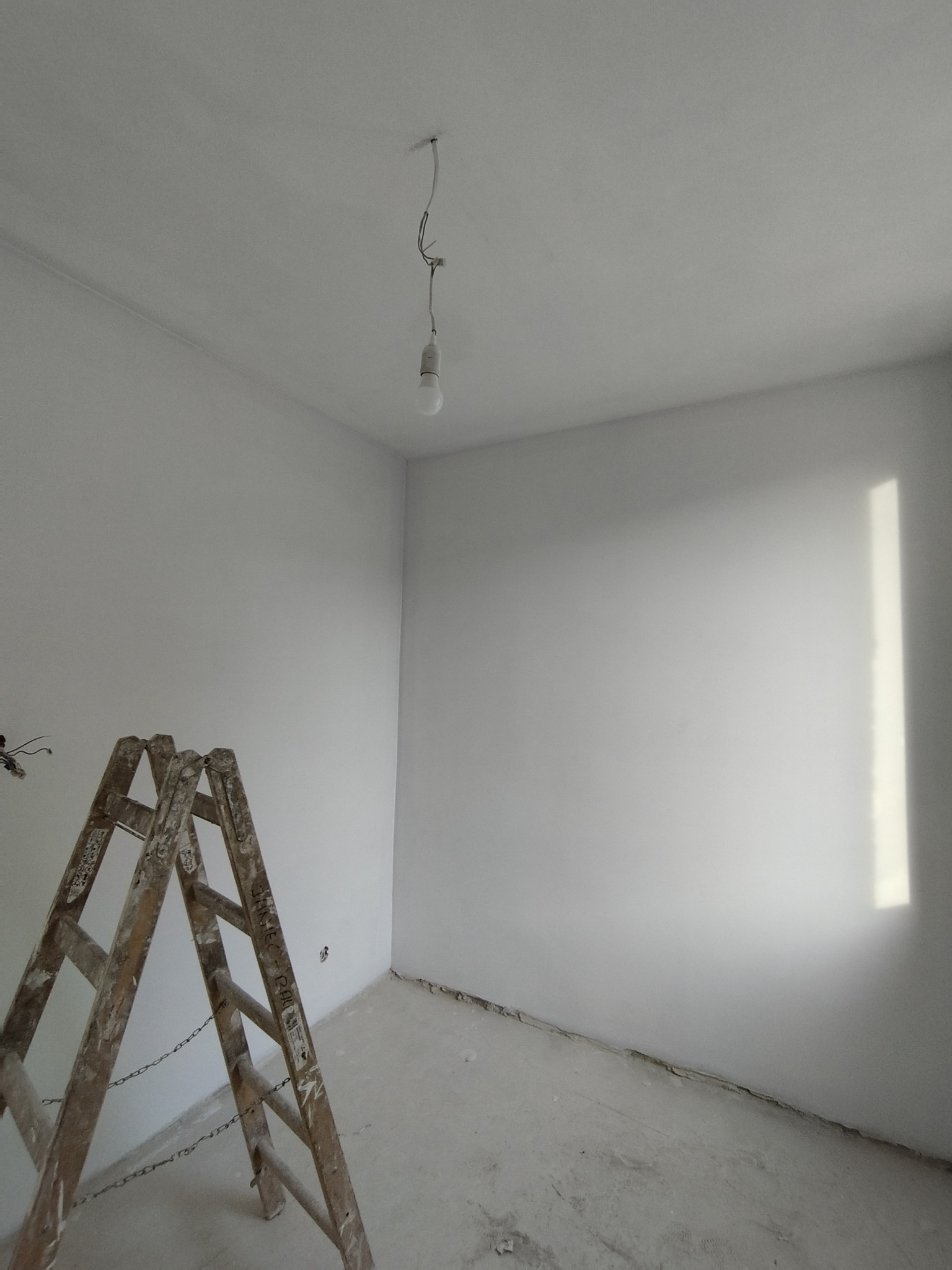 Pokój po szpachlowaniu w Szprotawie, widoczna drabina malarska, surowa żarówka i ślady po gładzi na ścianach.
