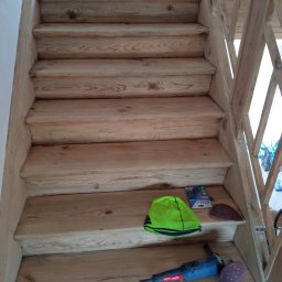 GREEN BUD ARTUR ZIELIŃSKI - Drewniane schody w trakcie renowacji, na stopniach szlifierka kątowa, papier ścierny, czapka robocza i butelka wody, widoczne ślady szlifowania.
