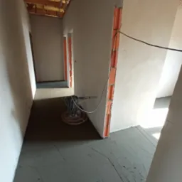 Wnętrze w trakcie wylewania posadzki jastrychowej z widoczną maszyną do zacierania i surowymi ścianami z instalacją elektryczną.