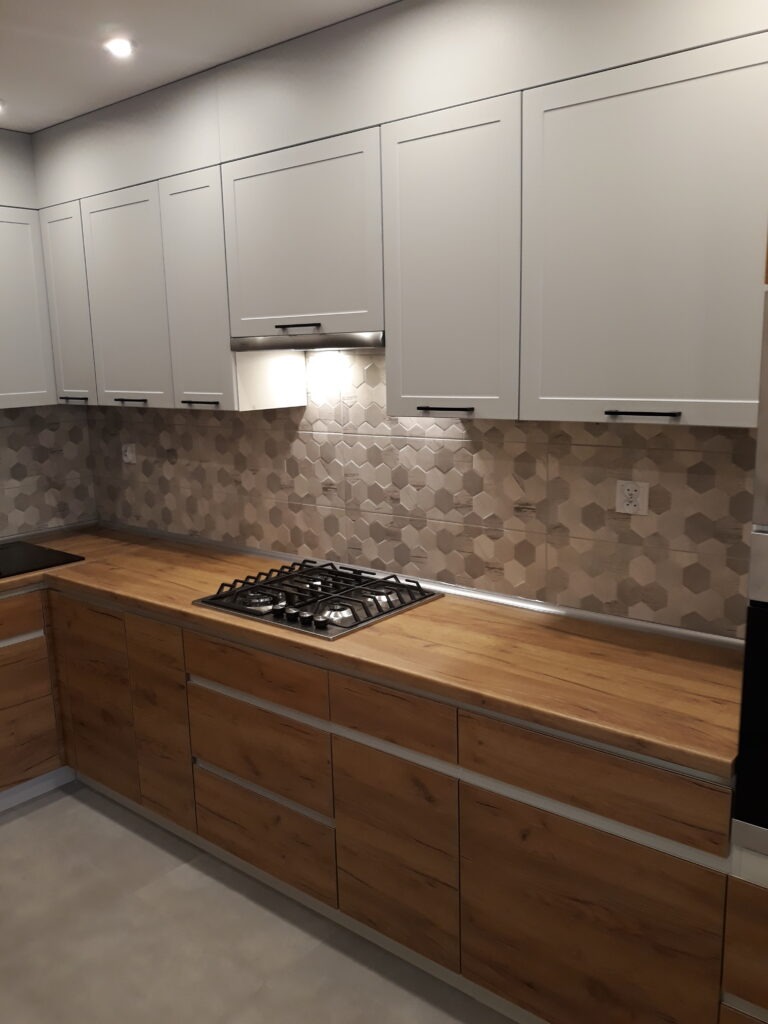 Nowoczesna kuchnia z drewnianymi szafkami dolnymi i białymi górnymi, heksagonalne płytki na ścianie, płyta gazowa.