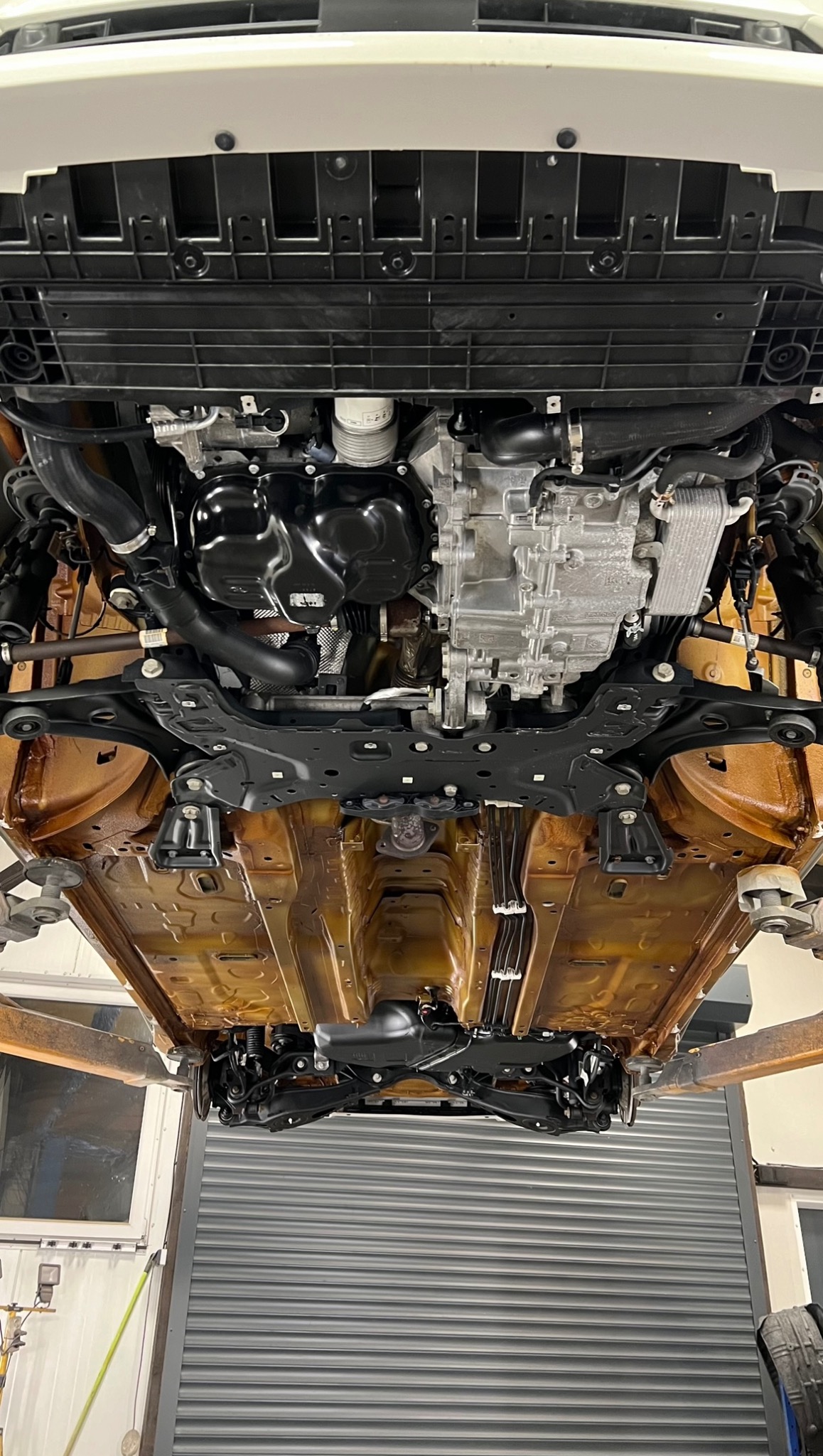 Podwozie samochodu po nałożeniu powłoki ochronnej, widoczne elementy zawieszenia i układu napędowego, pojazd podniesiony na podnośniku w warsztacie.