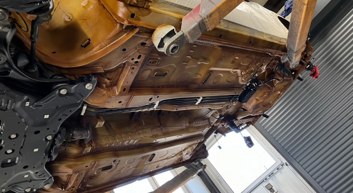 Podwozie samochodu po zabezpieczeniu antykorozyjnym, widoczne na podnośniku w warsztacie, z nowymi elementami zawieszenia w kolorze czarnym.