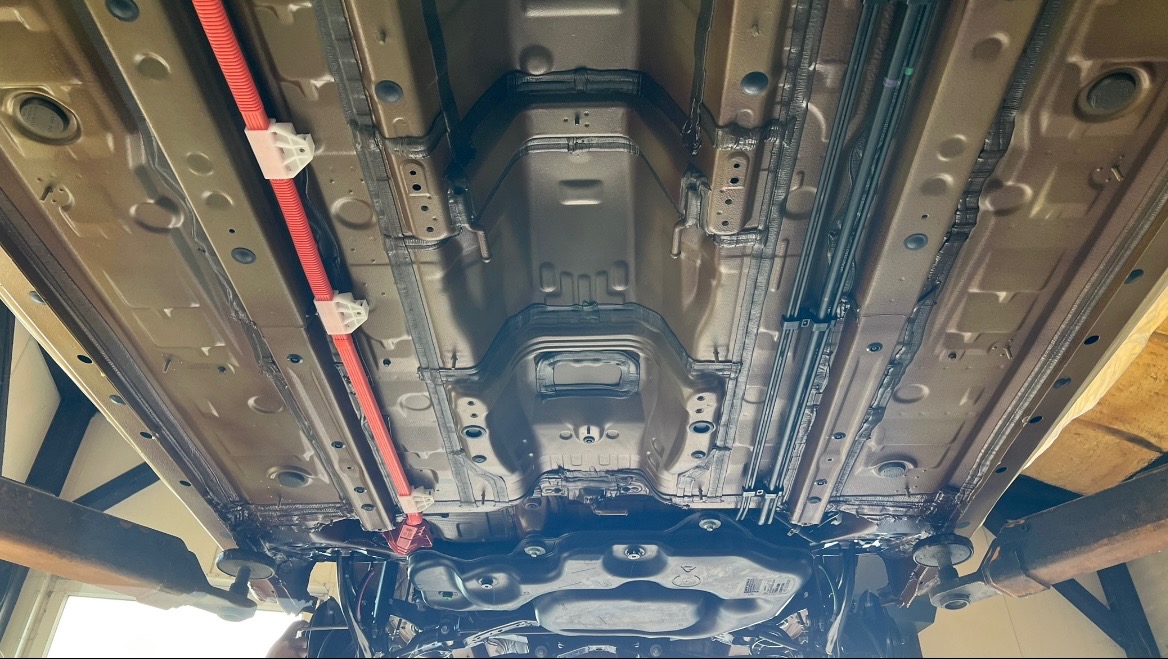 Podwozie samochodu po konserwacji antykorozyjnej, widok od spodu na podnośniku, z widoczną pomarańczową rurą ochronną na przewodach.