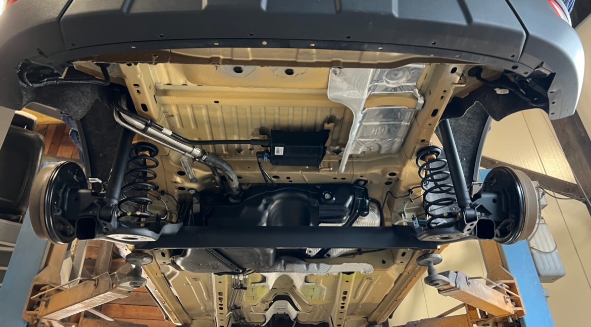 Spód samochodu na podnośniku warsztatowym, widoczne elementy zawieszenia, układ wydechowy i zabezpieczenia podwozia.