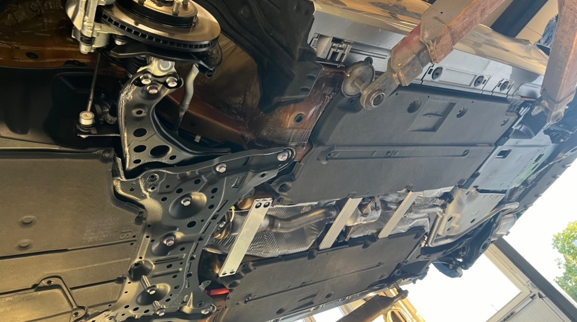 Widok podwozia samochodu na podnośniku, z widocznym układem wydechowym, elementami zawieszenia i osłonami podwozia.