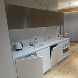 First Floor sp. z o.o - Nowoczesna kuchnia z białymi frontami i blatem z imitacją marmuru, otwartą zmywarką oraz drewnianą podłogą.