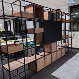 First Floor sp. z o.o - Regał biurowy z czarną metalową konstrukcją i drewnianymi elementami w odcieniach jasnego drewna, w tle widoczne biurka i krzesła biurowe.