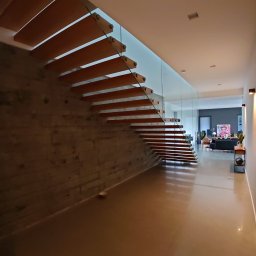 First Floor sp. z o.o - Nowoczesne schody drewniane wspornikowe z szklaną balustradą w minimalistycznym wnętrzu z betonową ścianą i polerowaną posadzką.