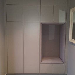 First Floor sp. z o.o - Szara szafa wnękowa z wbudowanym siedziskiem w przedpokoju, oświetlenie punktowe w suficie i brązowe płytki na podłodze.