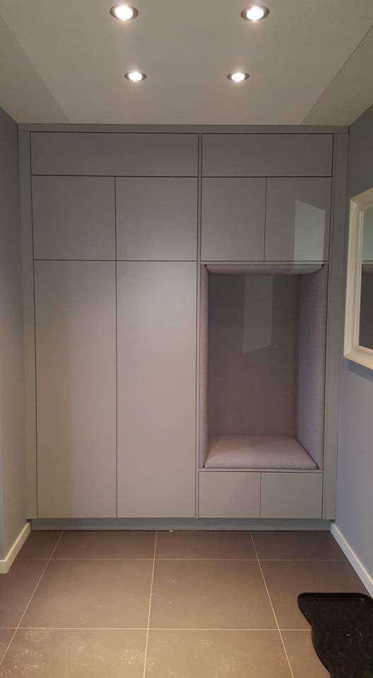 Szara szafa wnękowa z wbudowanym siedziskiem w przedpokoju, oświetlenie punktowe w suficie i brązowe płytki na podłodze.