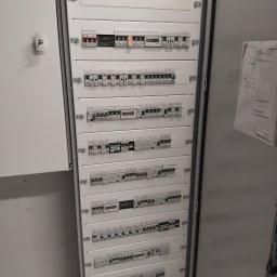 Torway sp. z o.o. - Rozdzielnica elektryczna z bezpiecznikami i wyłącznikami, widok z bliska na białą szafę sterowniczą z zainstalowanymi modułami. Widoczne opisy i etykiety na urządzeniach.