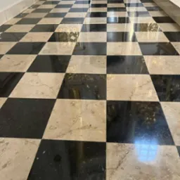 Błyszcząca, czarno-beżowa marmurowa podłoga w szachownicę w korytarzu, odbijająca światło z okna.