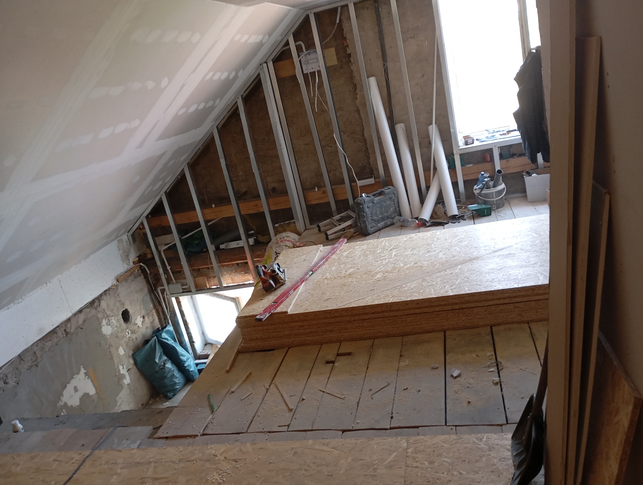 Poddasze w trakcie adaptacji: widoczne płyty OSB, konstrukcja szkieletowa, ocieplenie, narzędzia. Ujęcie z góry, ukazujące postęp prac wykończeniowych.