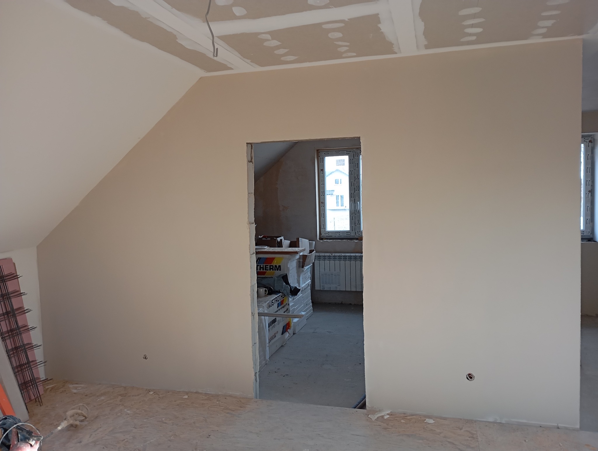 Poddasze po montażu płyt gipsowo-kartonowych i gładzi, widoczne puszki elektryczne, okno i materiały izolacyjne w tle. Ściany przygotowane do malowania.