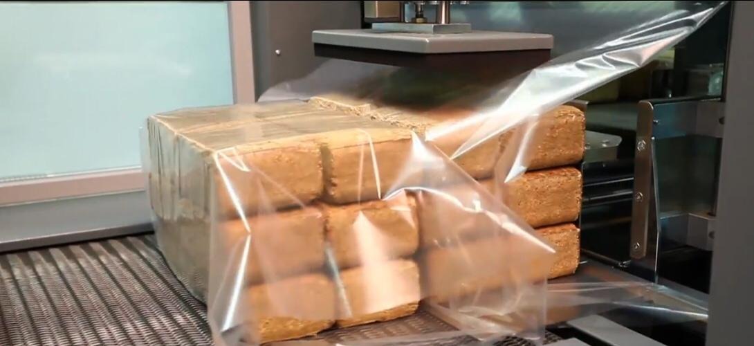 Automatyczny proces pakowania kostek opału w folię termokurczliwą na linii produkcyjnej.