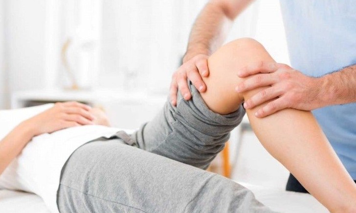 Pacjent w Puszczykowie leżący na leżance podczas badania stawu kolanowego przez terapeutę. Widoczna ręka terapeuty uciskająca kolano pacjenta.