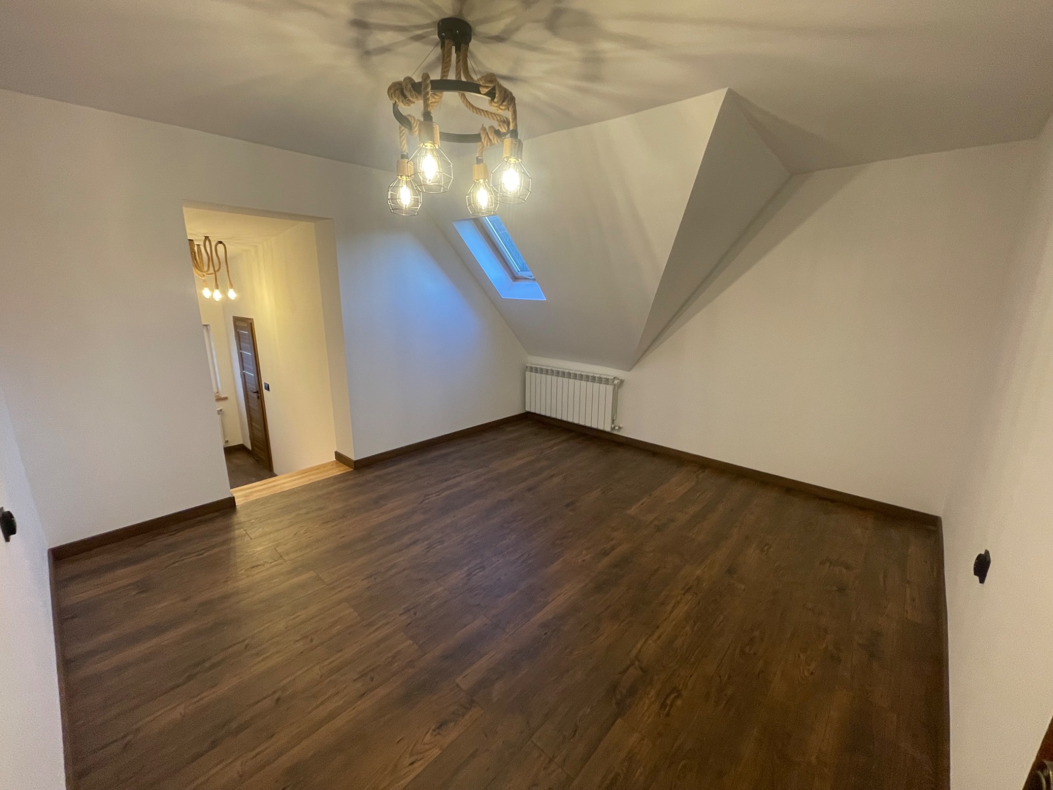 Poddasze z drewnianą podłogą, oknem dachowym i dekoracyjną lampą sufitową z linami, świeżo po pracach wykończeniowych.