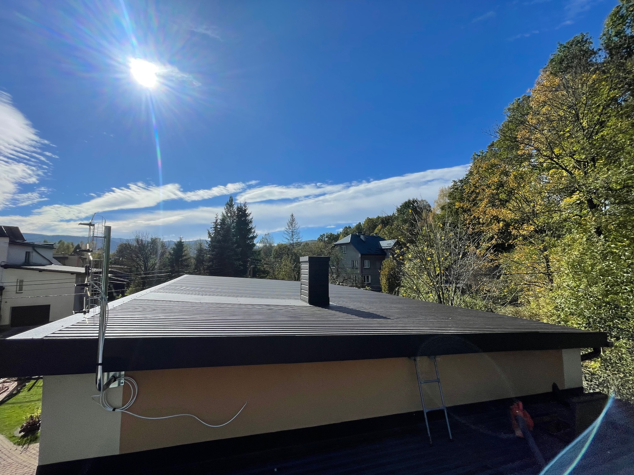 Nowoczesny, ciemny dach z blachy trapezowej w Makowie Podhalańskim, widok z góry w słoneczny dzień, antena satelitarna na boku budynku.