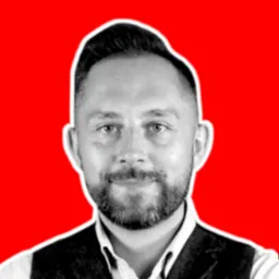 Portret mężczyzny z brodą w czarno-białej tonacji na intensywnie czerwonym tle, ubrany w kamizelkę.