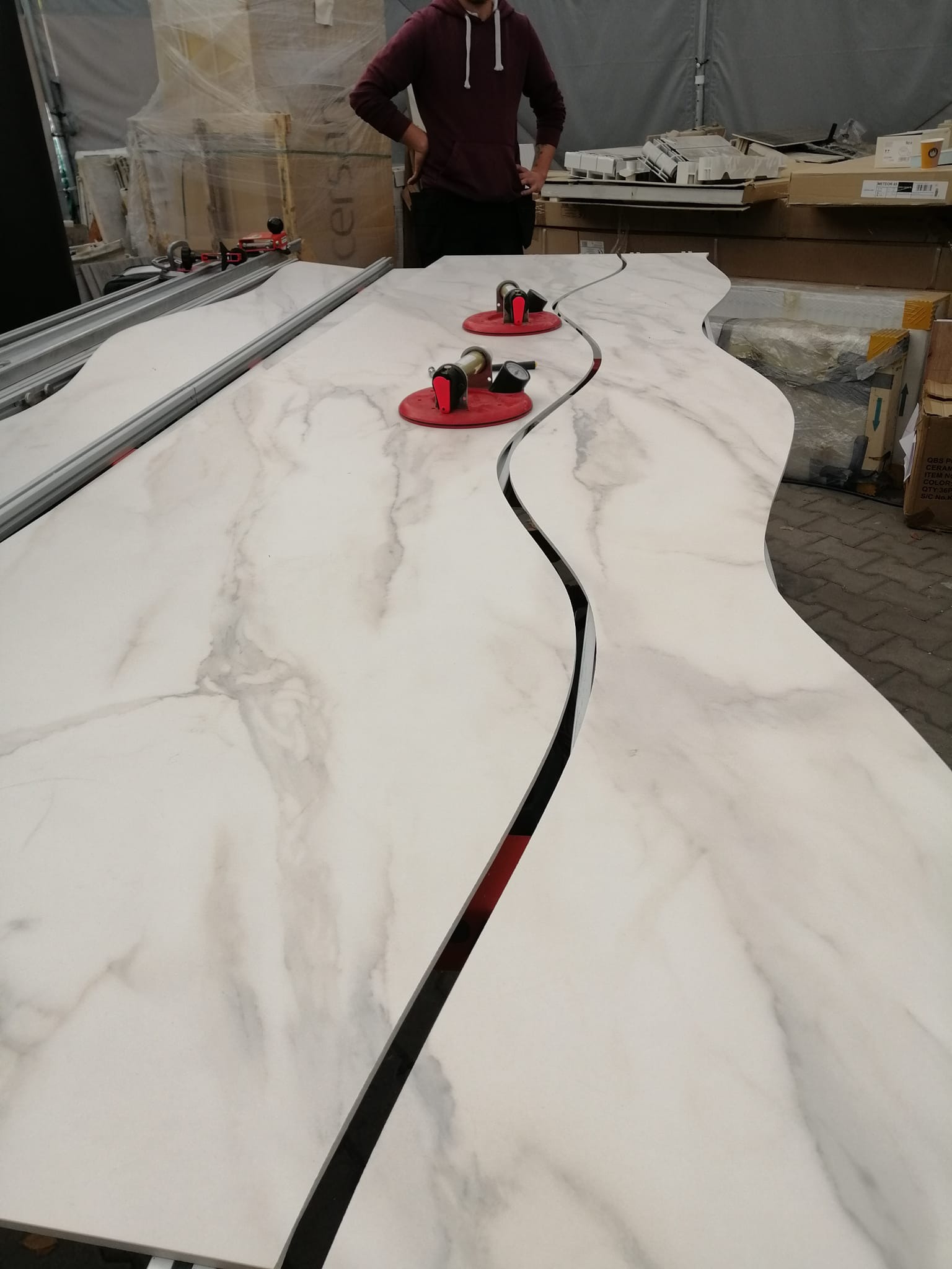 Przygotowane do montażu, wycięte blaty z płyty imitującej marmur, połączone przyssawkami, widoczne prowadnice do cięcia i osoba w tle.