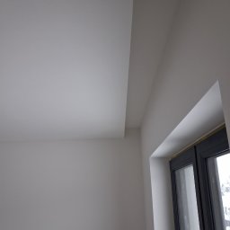 LUGIN-BUD Zbigniew Ługin - Gładka, biała ściana i sufit połączone pod kątem prostym, z widocznym oknem w czarnej ramie. Minimalistyczne wykończenie wnętrza, równomierne oświetlenie.