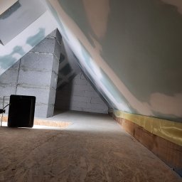 LUGIN-BUD Zbigniew Ługin - Poddasze w trakcie prac wykończeniowych: płyta OSB na podłodze, ściany z bloków i częściowo pokryte gładzią, widoczne zabezpieczenia folią. Oświetlenie halogenowe.