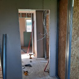 LUGIN-BUD Zbigniew Ługin - Montaż ścian działowych z płyt gipsowo-kartonowych w surowym wnętrzu. Widoczne profile, narzędzia i instalacja elektryczna. Prace wykończeniowe w toku.