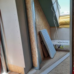 LUGIN-BUD Zbigniew Ługin - Skośne poddasze w trakcie zabudowy: metalowy stelaż, płyta OSB, częściowo zamontowana płyta gipsowa, okno dachowe, ocieplenie, wiertarka na podłodze.