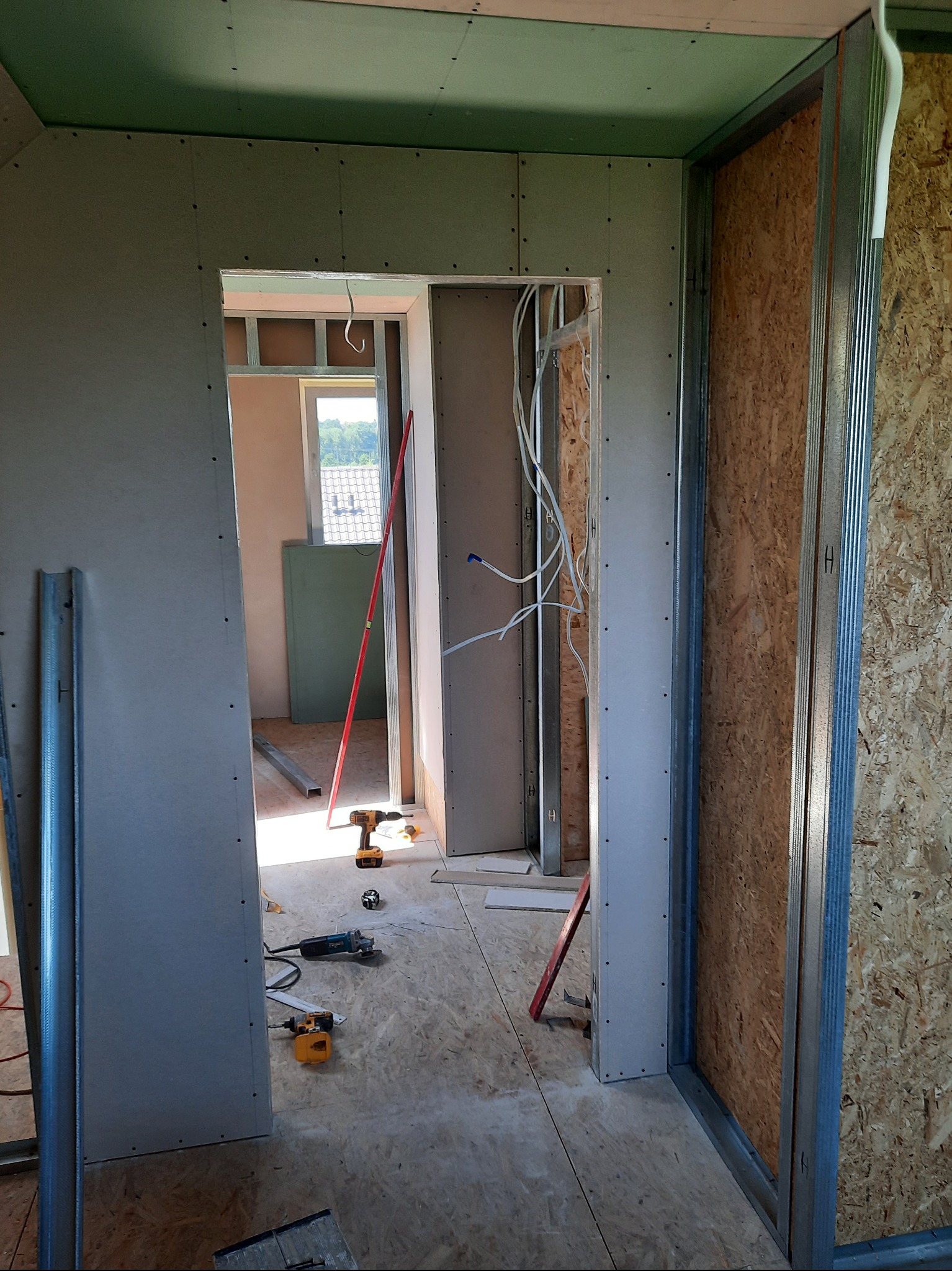 Montaż ścian działowych z płyt gipsowo-kartonowych w surowym wnętrzu. Widoczne profile, narzędzia i instalacja elektryczna. Prace wykończeniowe w toku.