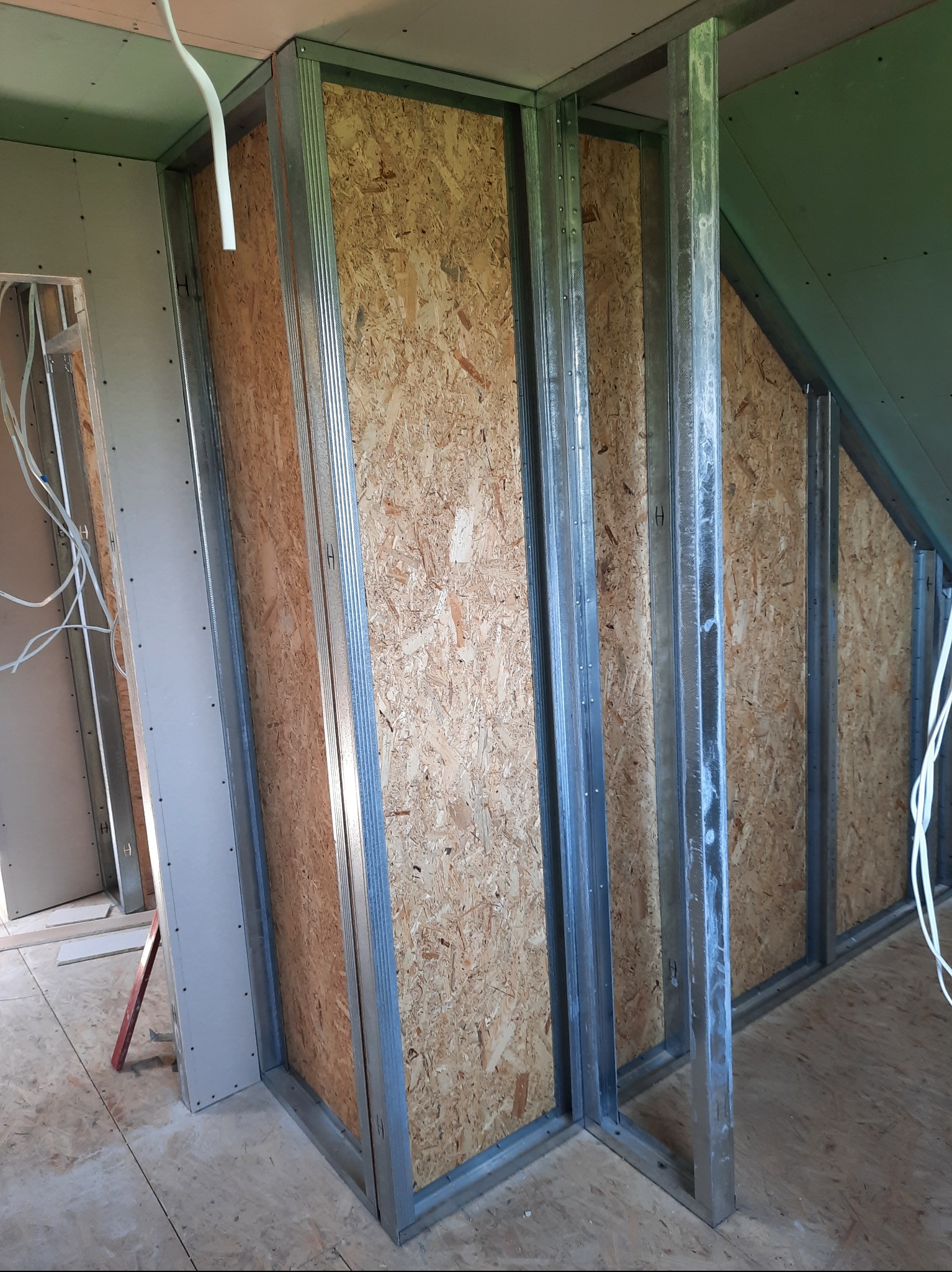 Konstrukcja ścianki działowej z metalowych profili i płyt OSB w surowym stanie, widoczne przewody elektryczne. Poddasze w trakcie prac wykończeniowych.