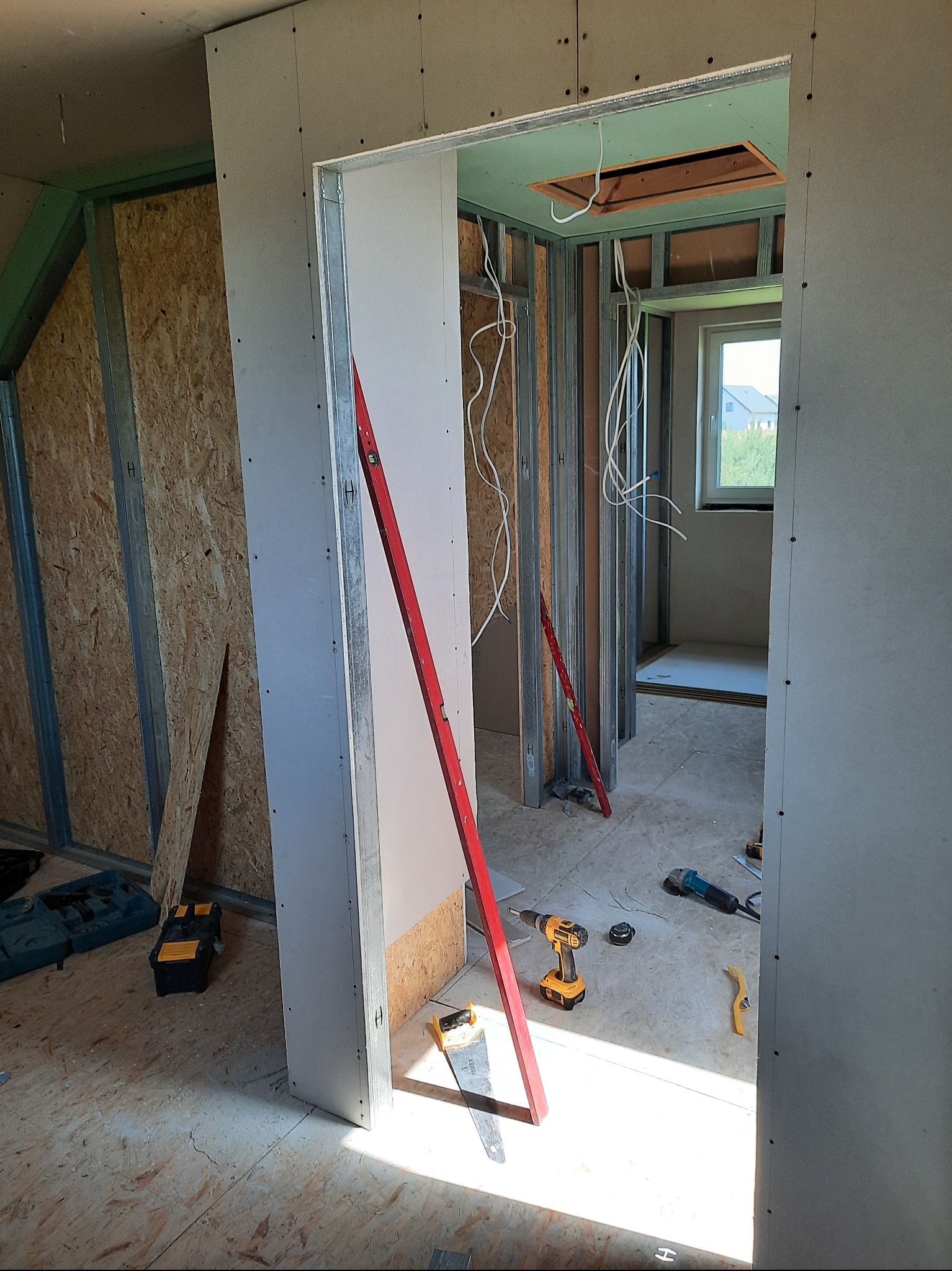 Montaż płyty karton gips na metalowym stelażu, widoczne narzędzia i poziomica. Prace wykończeniowe w nowym domu, surowy stan.