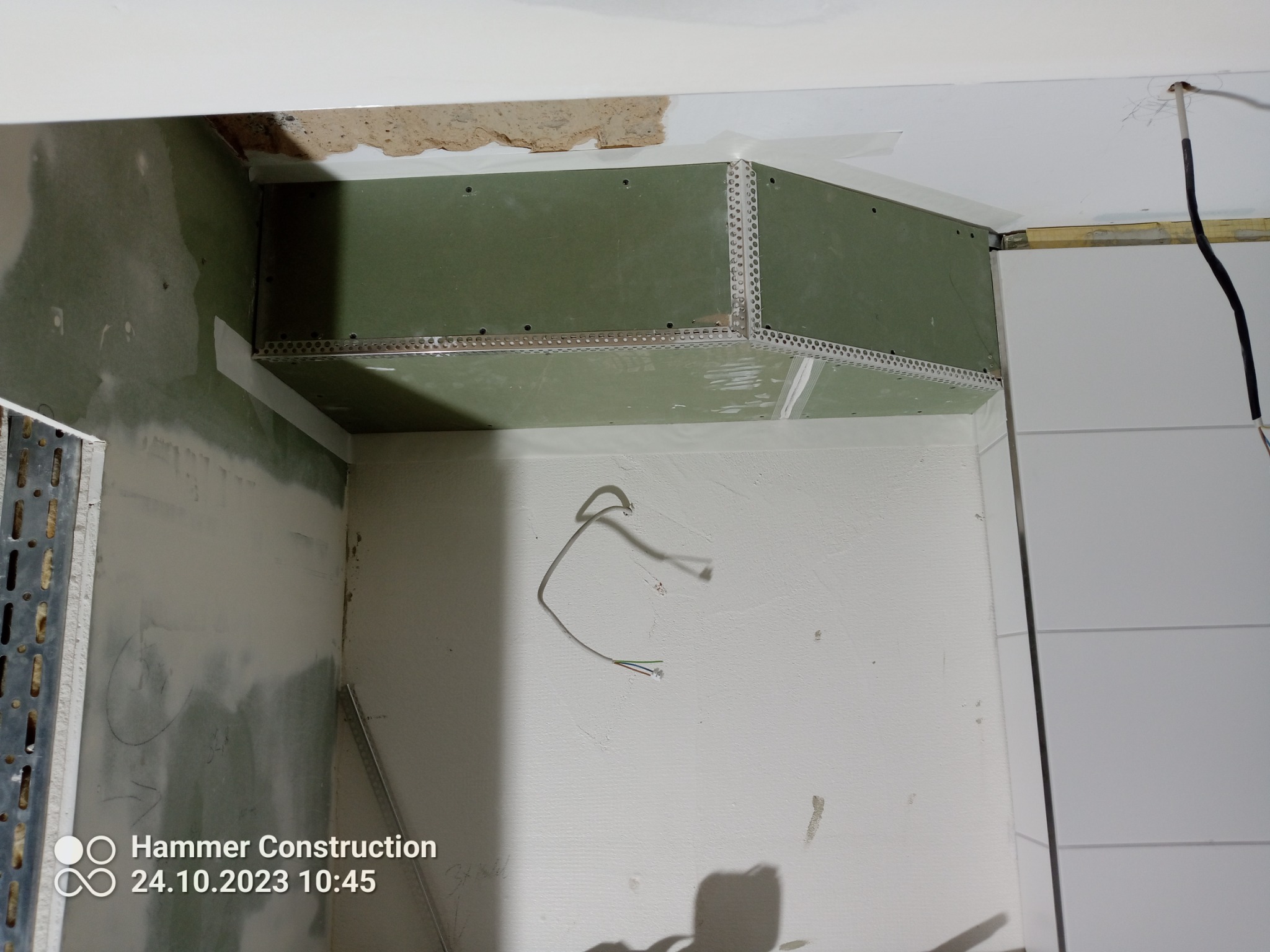 Narożnik pomieszczenia w trakcie prac wykończeniowych: zamontowane płyty gipsowo-kartonowe z metalowymi narożnikami, widoczne przewody elektryczne, ściany częściowo pokryte masą szpachlową.