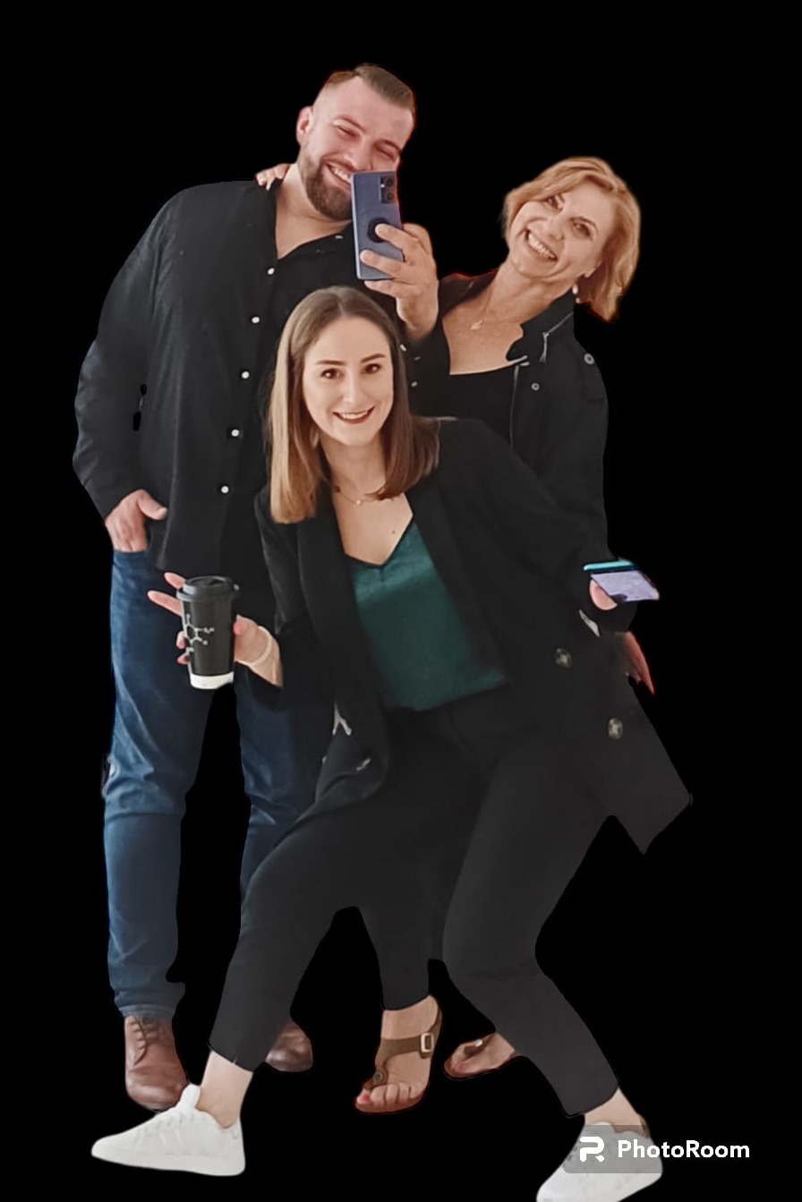 Trzy uśmiechnięte osoby pozują do selfie: mężczyzna robi zdjęcie telefonem, kobieta trzyma kartę, druga kobieta trzyma kubek z wzorem.