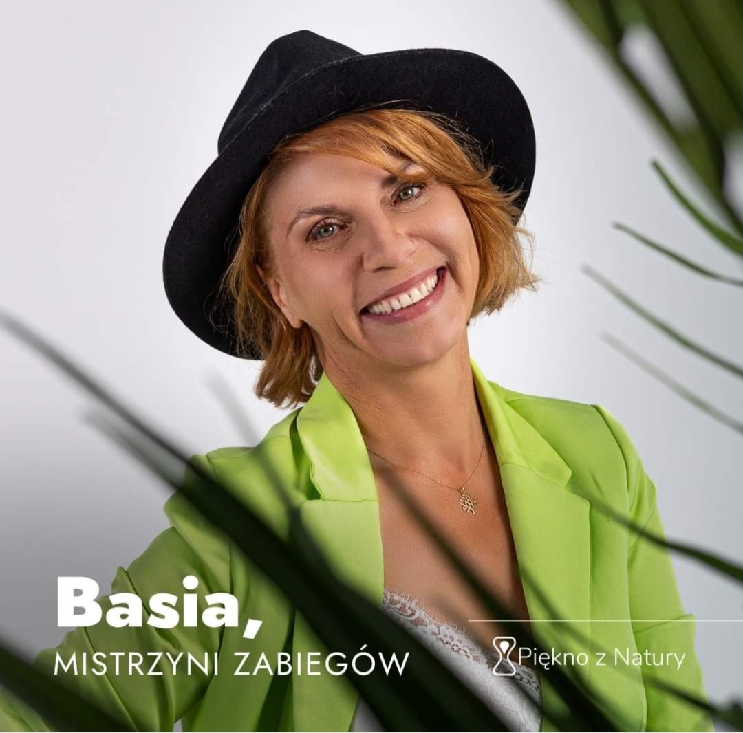 Portret uśmiechniętej kobiety w czarnym kapeluszu i limonkowym żakiecie, z napisem 'Basia, MISTRZYNI ZABIEGÓW' i logo 'Piękno z Natury' w tle, z elementami roślinnymi.