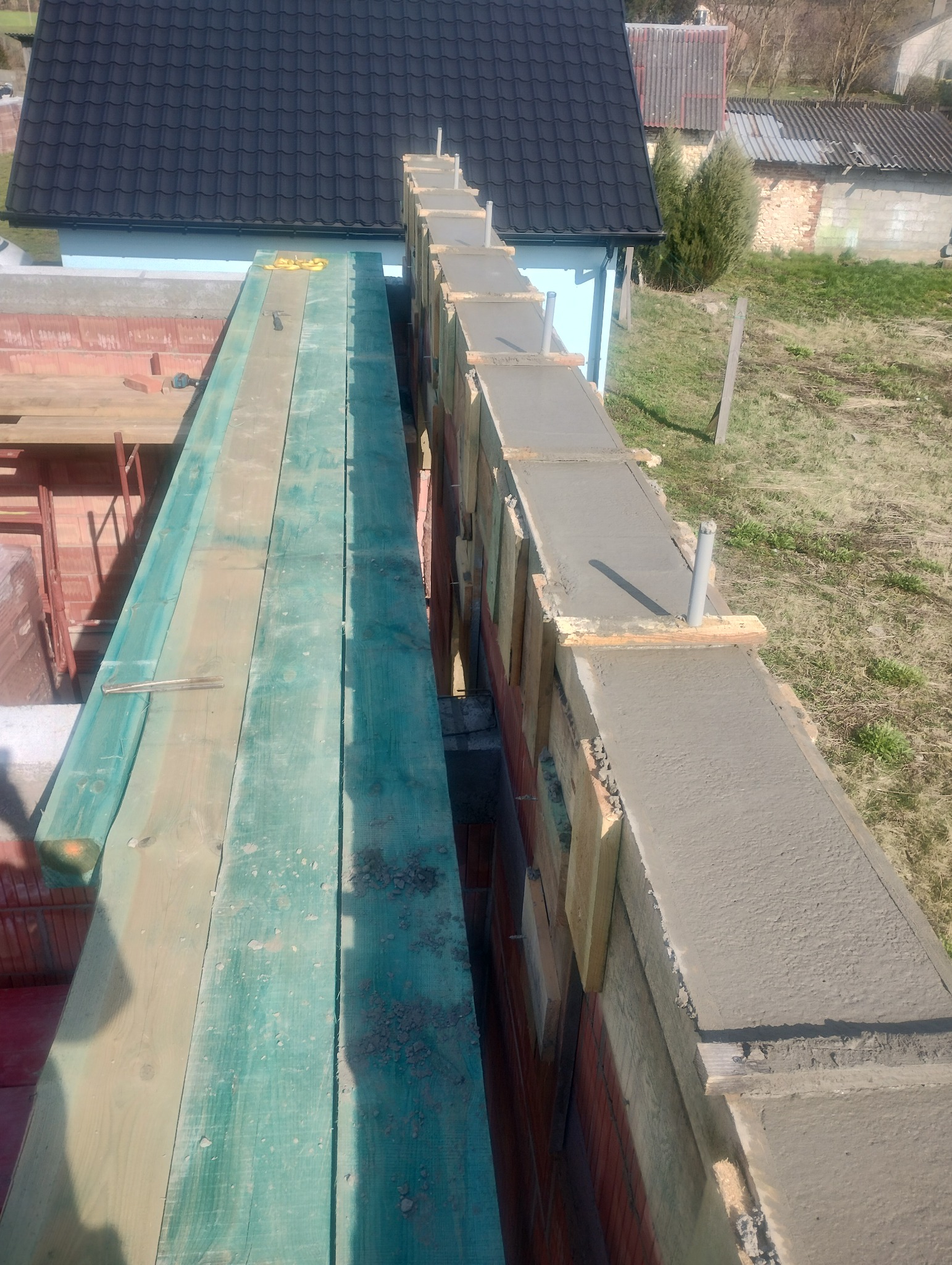 Wznoszenie muru z czerwonej cegły z szalunkiem i świeżo wylanym betonem na górze, widok z góry na budowę domu w słoneczny dzień.