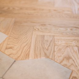 MP Parkiet Michał Piotrowski - Jasny parkiet ułożony we wzór jodełki francuskiej, przechodzący w heksagonalne płytki podłogowe. Kontrast materiałów i faktur, ciepłe odcienie drewna i chłodne płytki.