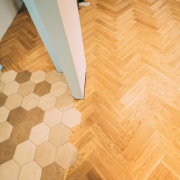 MP Parkiet Michał Piotrowski - Parkiet ułożony we wzór jodełki francuskiej, kontrastujący z heksagonalną mozaiką w odcieniach beżu i brązu. Widok z góry, jasne drewno, nowoczesne wykończenie.