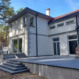 L.i.n.budservis - Nowoczesny dom jednorodzinny z białymi ścianami i szarymi elementami dekoracyjnymi elewacji, widok z zewnątrz na taras i schody wejściowe.