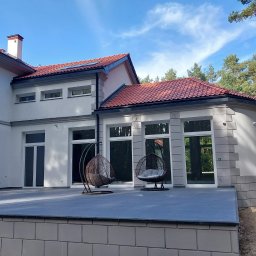 L.i.n.budservis - Nowoczesny dom z szarą elewacją, czerwonym dachem i tarasem z dwoma wiszącymi fotelami typu kokon