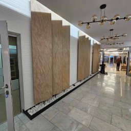 CICH-BUD CEZARY CICHOSZ - Montaż paneli dekoracyjnych w holu, widoczne pionowe płyty z teksturą kamienia, białe panele ścienne z delikatnym wzorem fal, dekoracyjne białe kamienie u podstawy ściany, eleganckie oświetlenie...