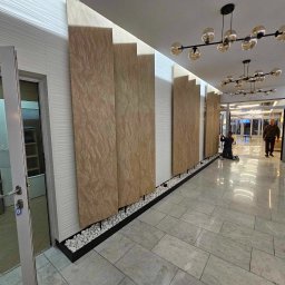 CICH-BUD CEZARY CICHOSZ - Korytarz biurowy z dekoracyjnymi panelami ściennymi imitującymi kamień, podświetlanymi od góry, z białymi kamykami u podstawy, oraz nowoczesnymi lampami sufitowymi.