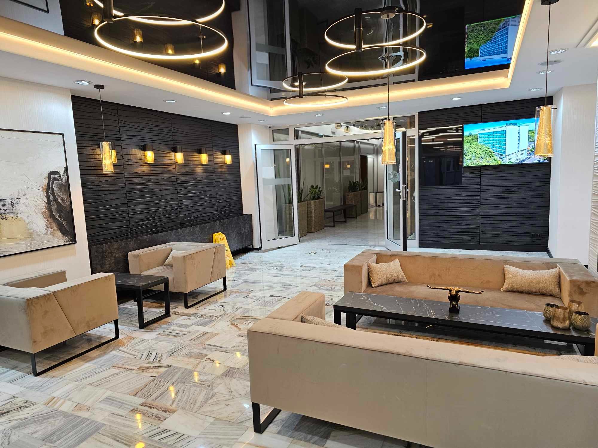 Eleganckie lobby biurowca z marmurową podłogą, beżowymi sofami, czarnymi ścianami z fakturą fal i nowoczesnym oświetleniem, w tym okrągłymi lampami sufitowymi i wiszącymi lampami w kształcie tub