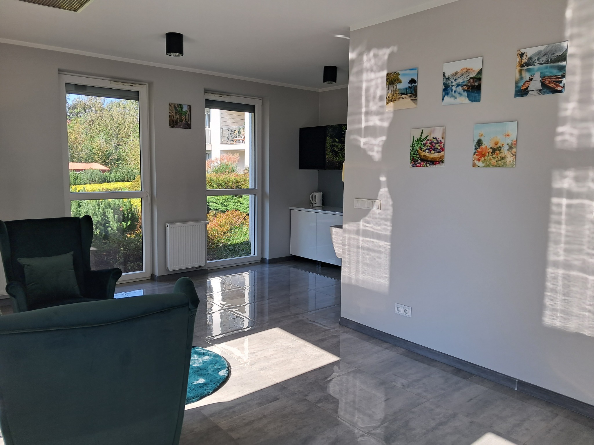 Wnętrze pokoju z dwoma zielonymi fotelami, na ścianie wiszą obrazy, widok na ogród przez okno.